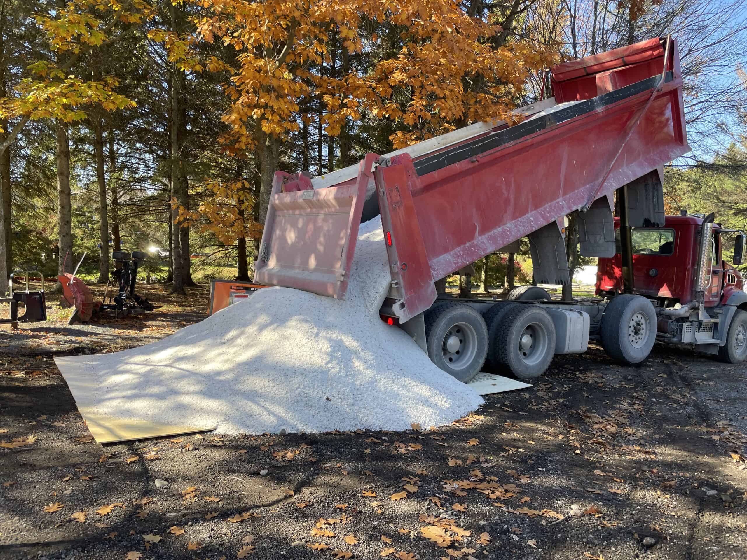 a red dump trunk dumping a white fertilizer mixture on dirt