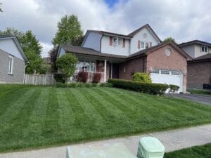 a freshly mowed front yard outside a two-story brick house with a covered porch and privacy fence