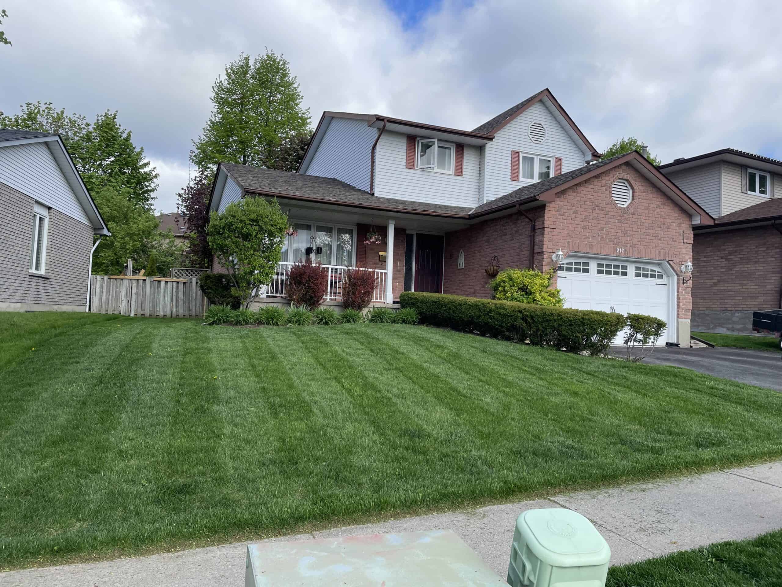  a freshly mowed front yard outside a two-story brick house with a covered porch and privacy fence